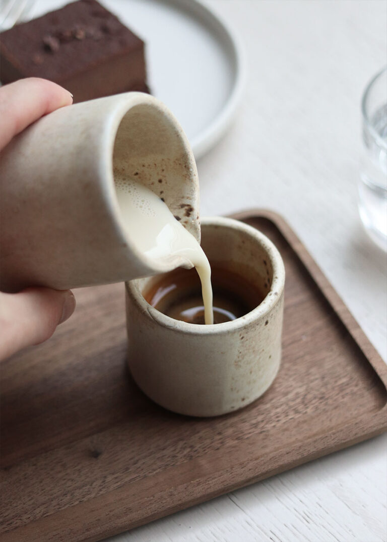 Aus einer kleinen Karaffe wird Milch in einen Espresso gegossen